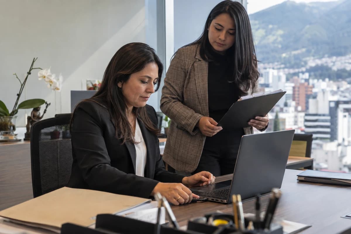 Oficina en Quito: la representante legal de una empresa conecta su token de firma electrónica a la laptop mientras un asistente espera a su lado con una carpeta.