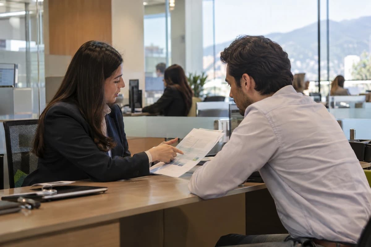 Oficina de una agencia bancaria en Quito: un empresario escucha a un oficial de crédito que le explica una hoja impresa al otro lado del escritorio.